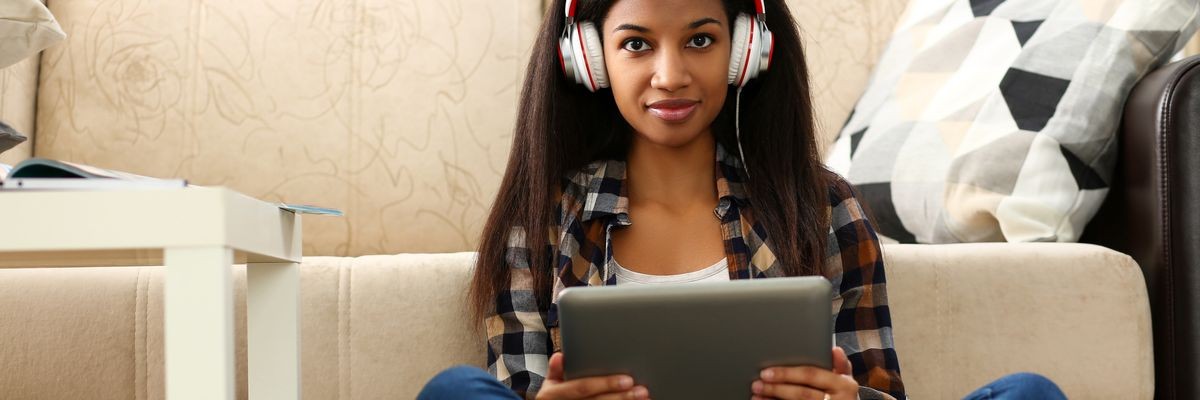 Black ordinary female american teen portrait at home sofa remote education concept. Girl hold tablet in hand music apps teacher checks homework online university library learning foreign languages